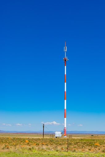 A vertical shot of a red and white cell tower in the countryside in South Africa