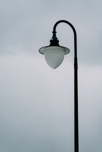 A vertical shot of a black and white lamppost against a blue cloudy sky