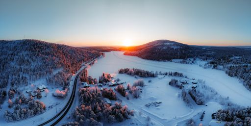 An aerial view of a frozen lake in Norway surrounded by trees on a cold winter day during the sunset