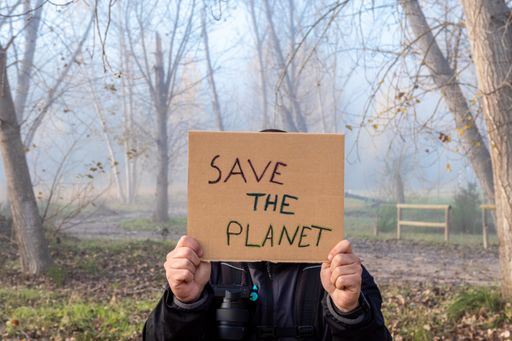 The Male hands hold a cardboard sign with the slogan Save the Planet with the forest in background