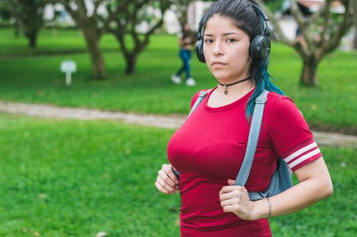 A young Hispanic female with blue hair listening to music with her wireless headphones in a park