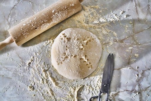 A top view of a scoured dough sprinkled with flour and a wooden rolling pin and kitchen scissors on a marble table