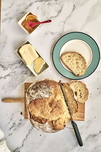 A top view of a sliced freshly baked bread on a wooden board with butter  and marmalade