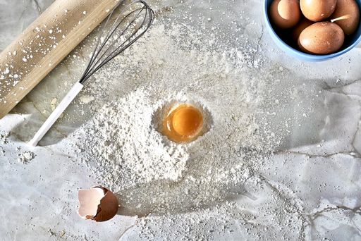 A top view of a mound of floor with an egg, a beater and a wooden rolling pin
