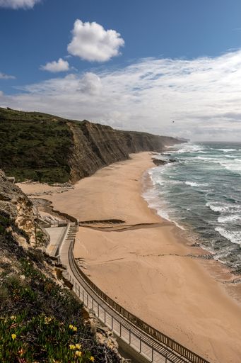 A beautiful view of sandy beach with a pathway on the cliff