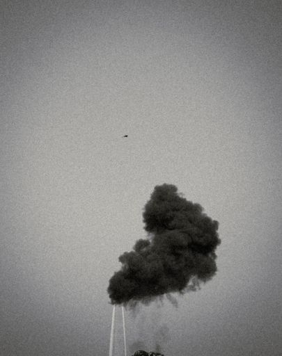 A vertical grayscale shot of a dark smoke in the background of a sky.