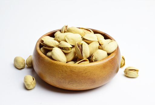 A wooden bowl with tasty pistachios isolated on a white background - dried seeds