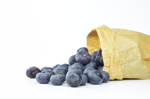 Fresh ripe blueberries scattered and inside a kraft paper bag on a white background