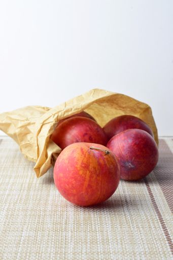 Fresh ripe plums inside a kraft paper bag on a tablecloth