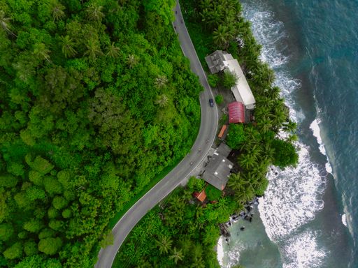 An aerial view of the small town with curved road surrounded by high dense trees and blue sea