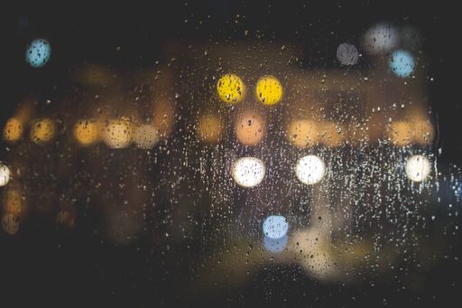 A closeup of raindrops on a clear glass window with blurred lights in the background