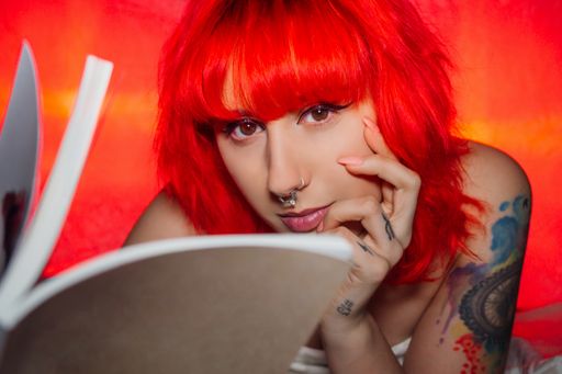 A woman with red hair and a nose piercing reading a book