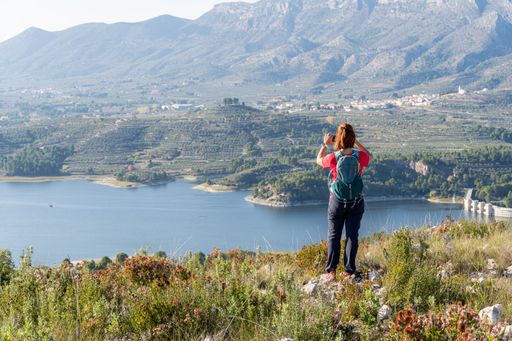A hiker photographing the mesmerizing views of the lake and green hills in spring