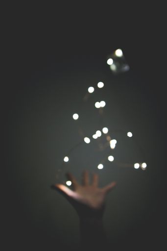 A vertical blurred shot of a person's hand reaching towards the lights with a dark background