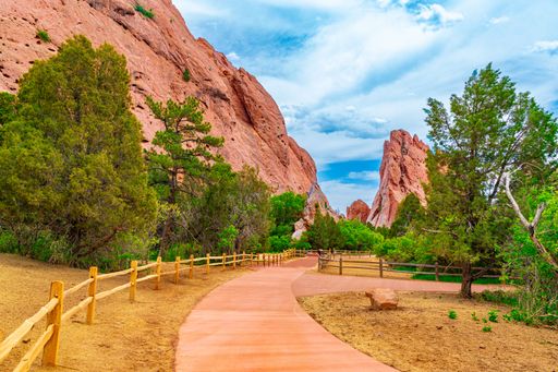 A scenic pathway at Garden of the Gods, Colorado Springs, with red rock formations and lush greenery under a vibrant blue sky.
