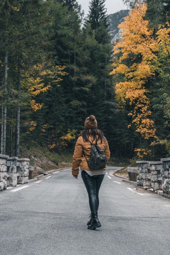 Earth tones photo of female hiker standing in middle of road in forest. Moody tones of beautiful nature with fall colors.