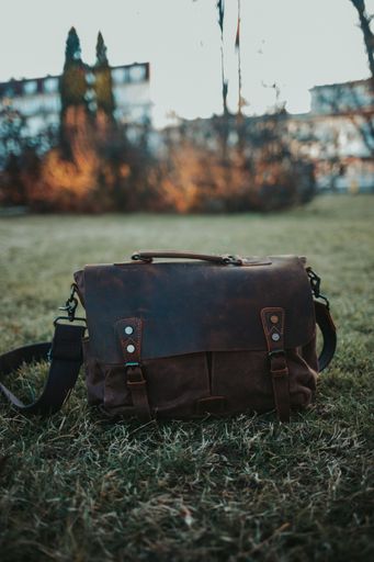 A vertical closeup shot of a brown leather satchel on the green grass