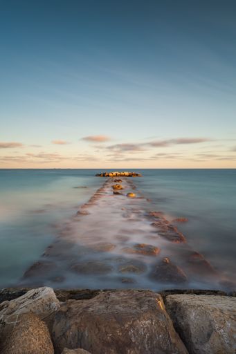 A coastal breakwater overflow with water during high tide at sunset