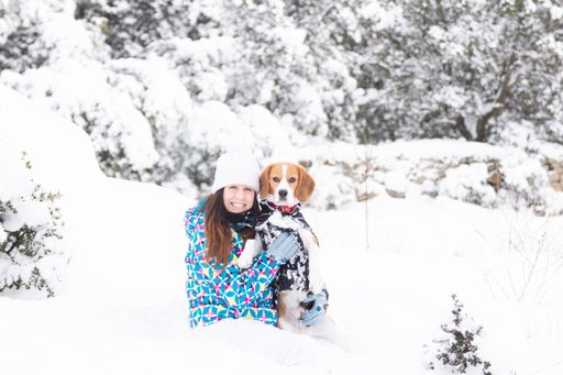 A young woman smiling, hugging her beagle dog, and having fun in a beautiful snowy forest
