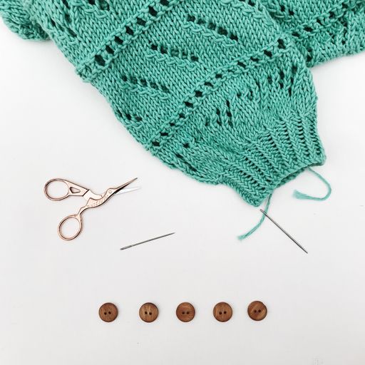 A top view of a piece of fabric, scissors, needles, and buttons on a white background