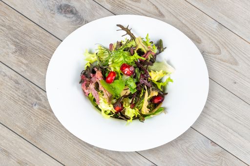 A closeup shot of a delicuoush vegan salad with pomegranate in a white plate on a wooden table