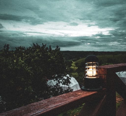 A closeup shot of a lamp on the wooden railing with dense greenery background at sunset