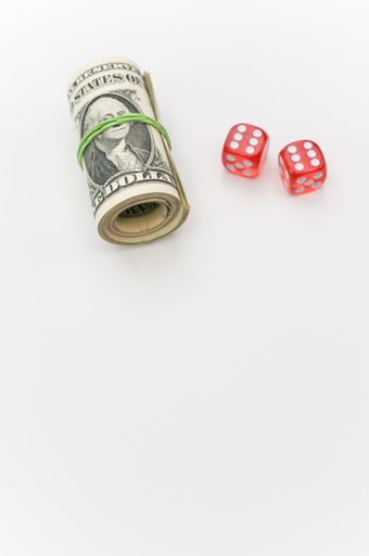 US dollar banknotes rolled up and red dice on a white tabletop with text space