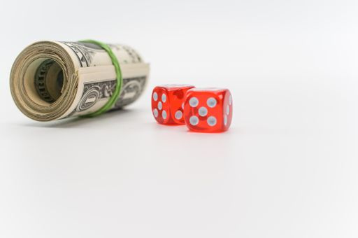 US dollar banknotes rolled up and red dice on a white tabletop with text space