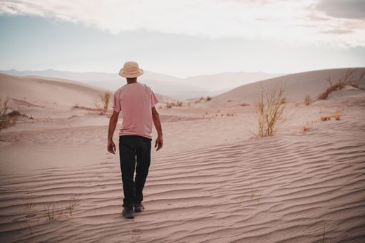 A man walking through a serene desert landscape with rolling sand dunes under a partly cloudy sky.
