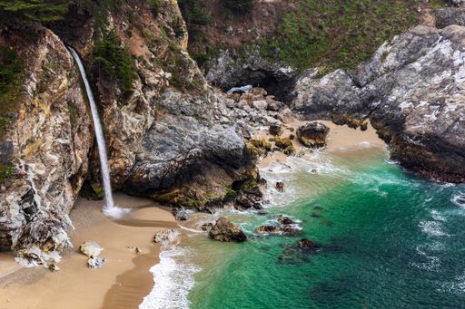 A beautiful view of a waterfall crashing onto a beach in a secluded cove