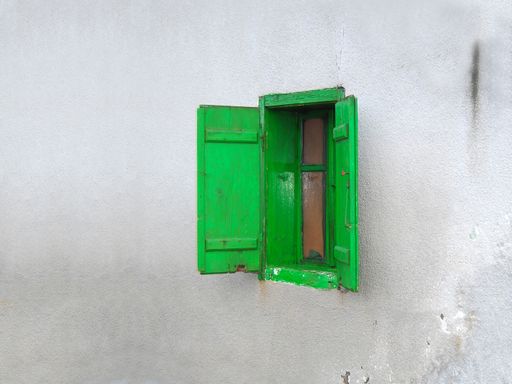 An old wooden window with green shutters on the wall of an old house in Jermenovci, Banat, Serbia