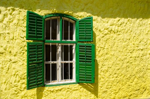 An old wooden window with metal bars and green shutters on a yellow wall in Dobrica, Banat, Serbia