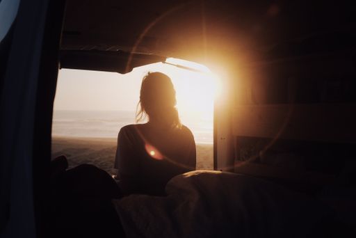 A mesmerizing view of an adult female watching the sunset from a camper van at the beach