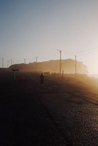 A vertical shot of an adult female walking down the street at sunset