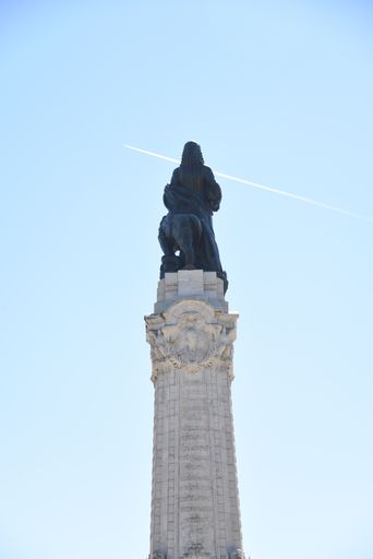 A vertical low angle shot of Eduardo VII's statue in Lisbon, Portugal and a flying airplane in the sky