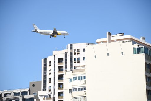 A view of an airplane flying over the buildings in the clear blue sky captured on a sunny day
