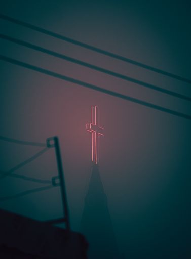 Red glowing cross atop an old church building during a foggy evening