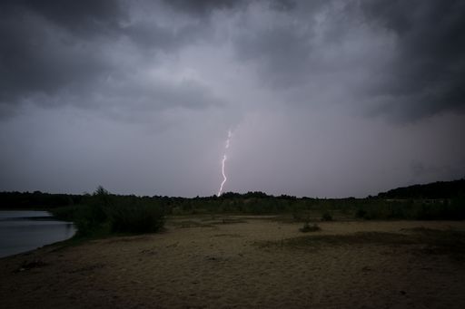 A landscape view of a field near a lake and lightning in the sky