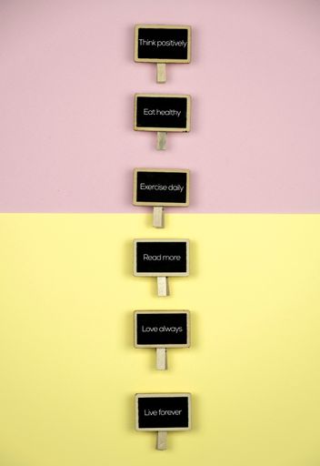 A vertical shot of wooden blackboards with motivational phrases on a pastel pink and yellow background