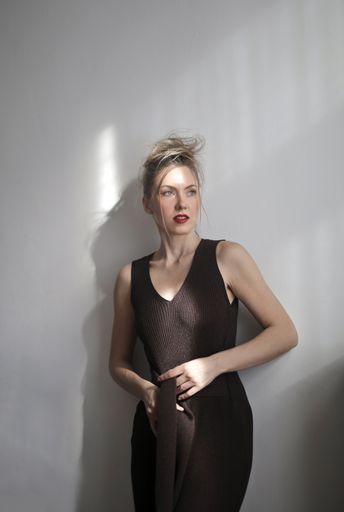 A vertical shot of an attractive female wearing black jumpsuit and red lipstick leaning against wall