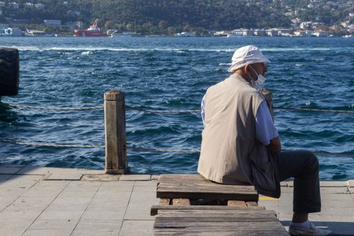 A vertical shot of a man in a medical mask relaxing on a wooden board at the docks in Istanbul, Turkey