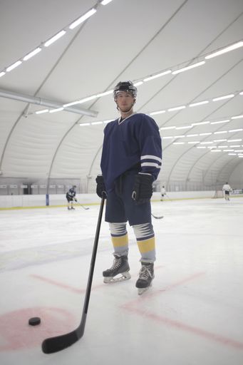 A selective focus shot of an attractive male ice hockey player in blue uniform hockey stick in his hand