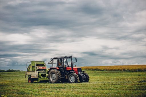 A horizontal view of a tractor on a green grass field under the blue cloudy  sky