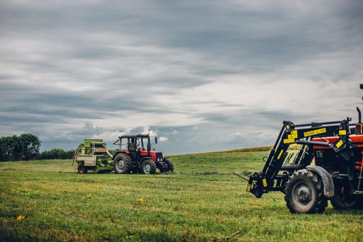 A horizontal view of tractors harvesting grass under cloudy sky