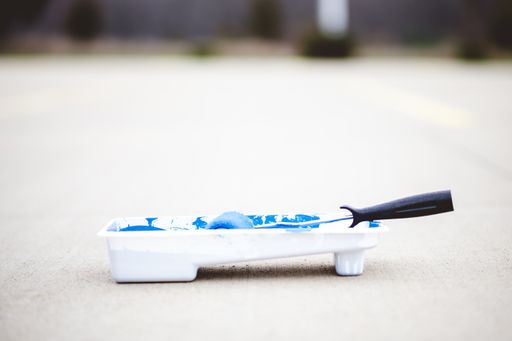 A paint roller in a tray with blue paint on a concrete ground