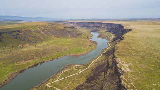 A wide shot of a river flowing among green hills under a clear sky