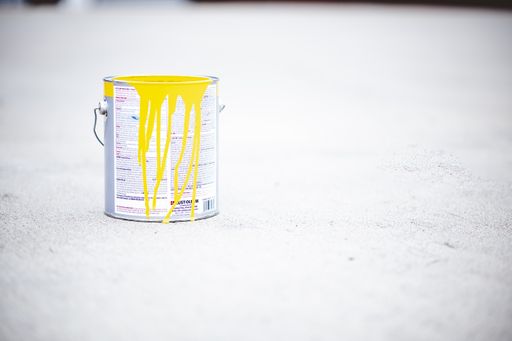 A view of a metal can with yellow paint on it placed on the asphalt of a street