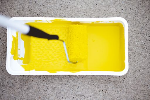 A top view of a paint roller in tray with yellow paint on a concrete ground