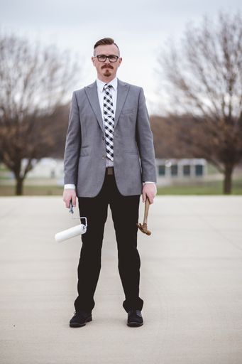 A vertical shot of a male wearing a suit while holding a hammer and a paintbrush on the street