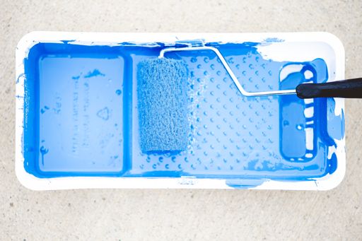 A top view of a paint roller in tray with blue paint on a concrete ground